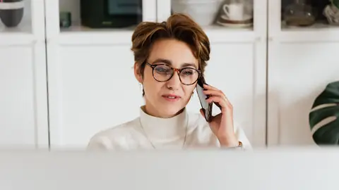 Une femme à lunettes au téléphone, attentive, à son bureau