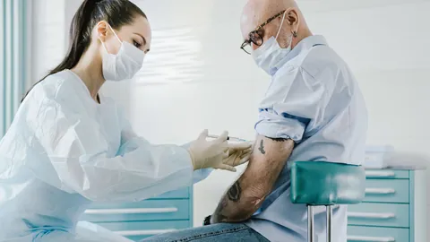 Une soignante masquée vaccine au bras un homme âgé, masqué lui aussi